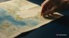 Mano colocando una chincheta ámbar sobre un mapa de papel de la costa